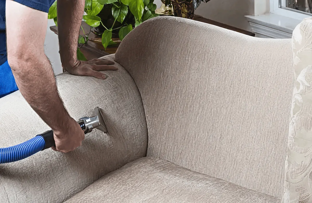 Professional upholstery cleaner deep-cleaning a fabric sofa with a handheld extraction tool and hose, Reno, NV.